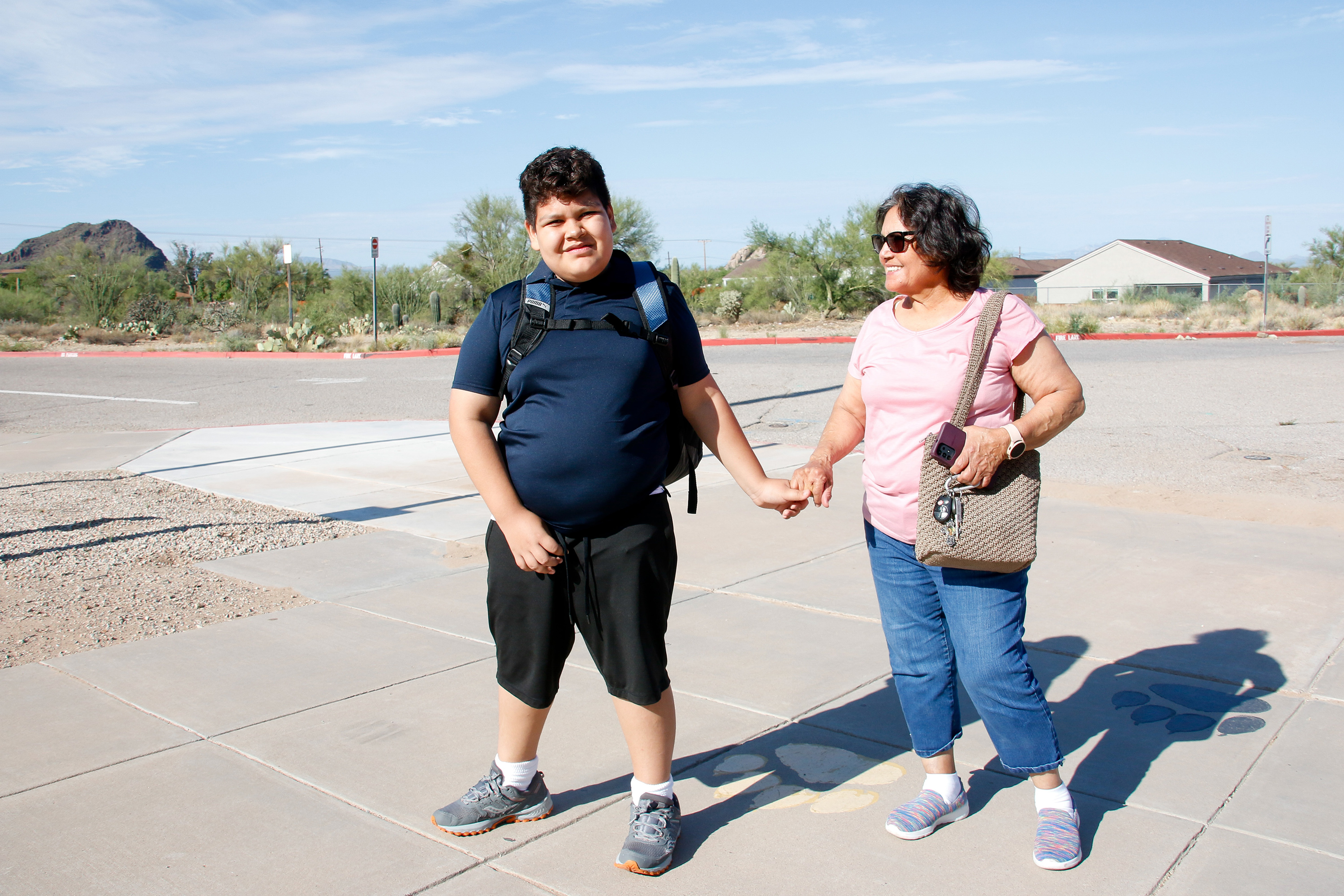 A middle school boy holds hands with his mom before starting his first day of school