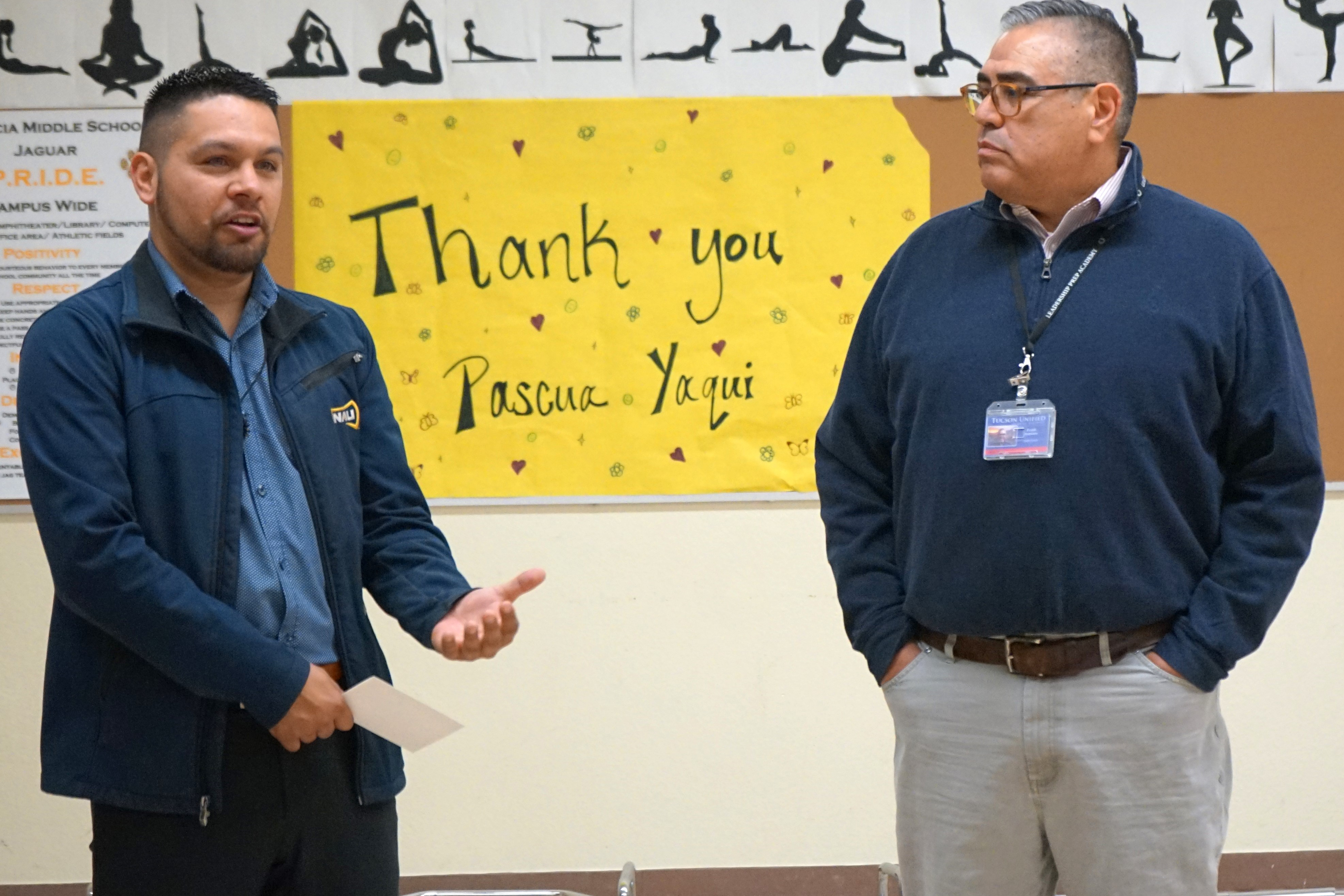 Two men stand in front of a banner reading Thank You Pascua Yaqui