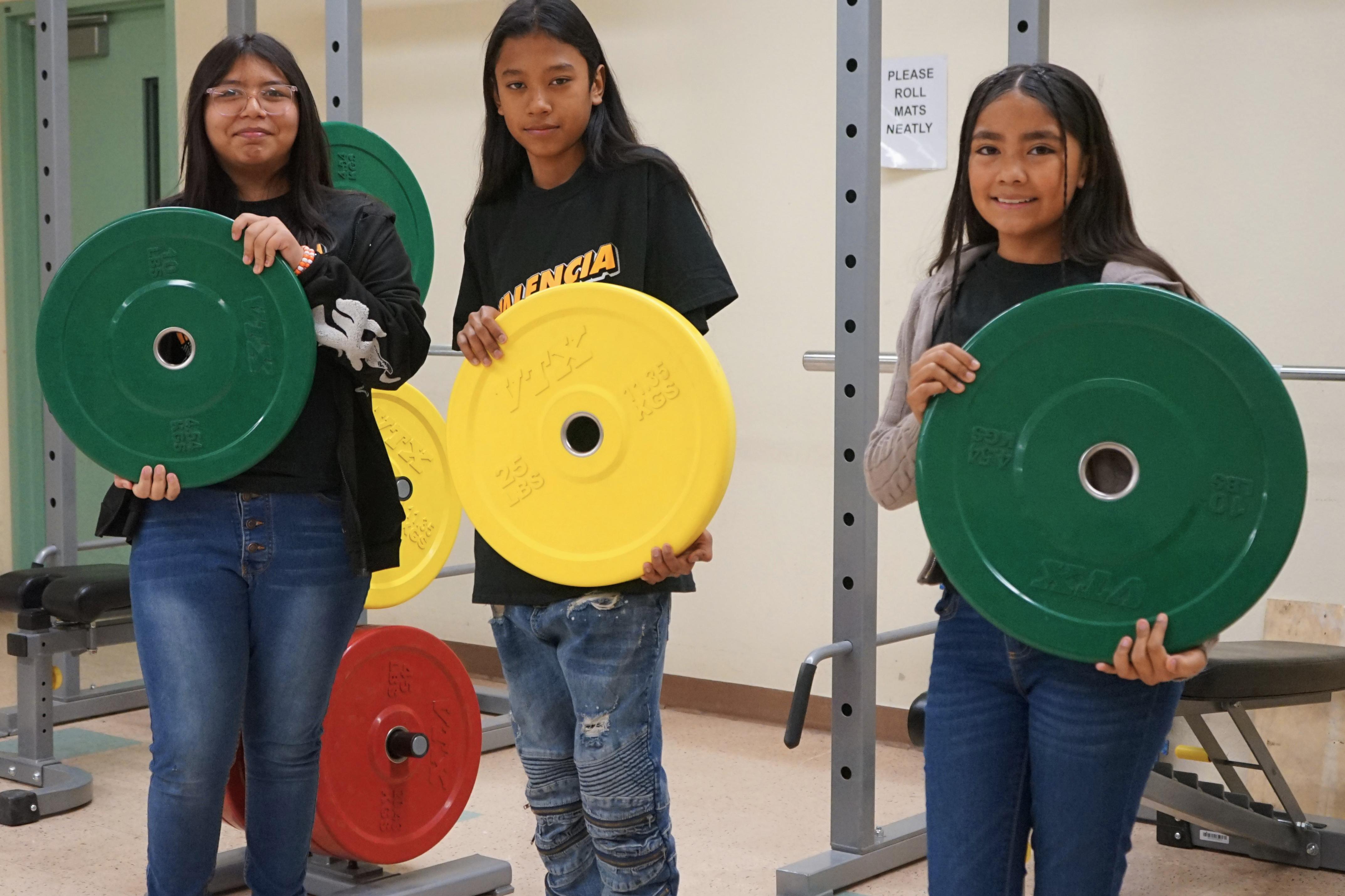 Three students hold up green and yellow weight plates